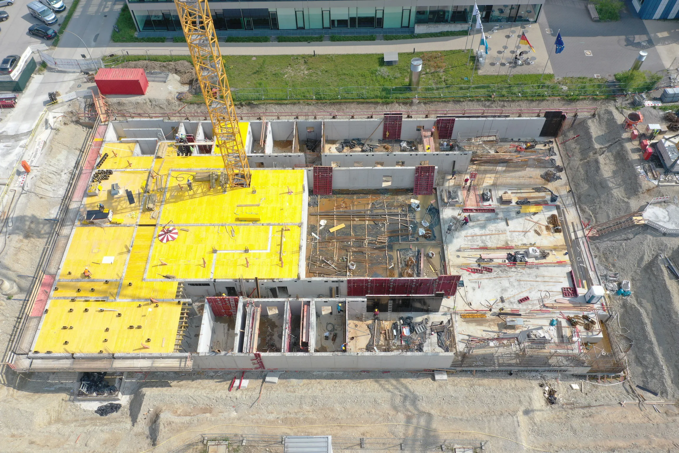 Rohbau von oben mit gelben Deckenschalungen, Betonwänden und einem Baukran.