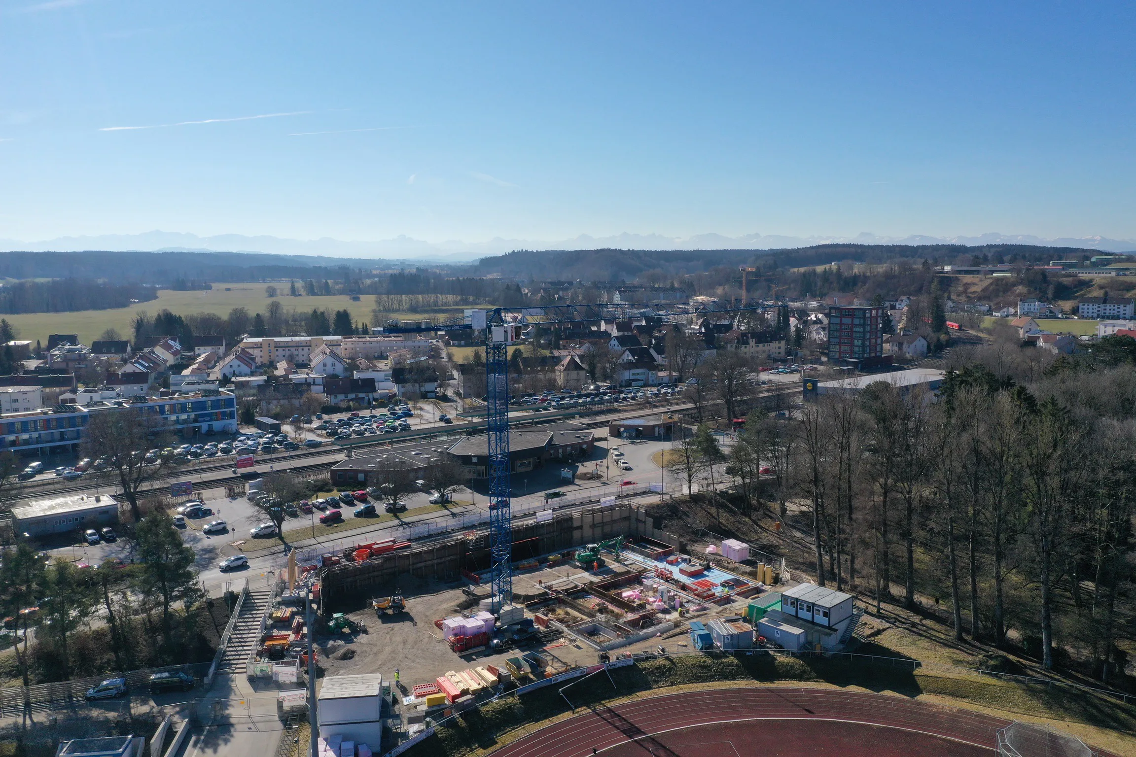 Weitläufige Stadtansicht mit einer Baustelle und Baukran im Vordergrund sowie Hügeln am Horizont.