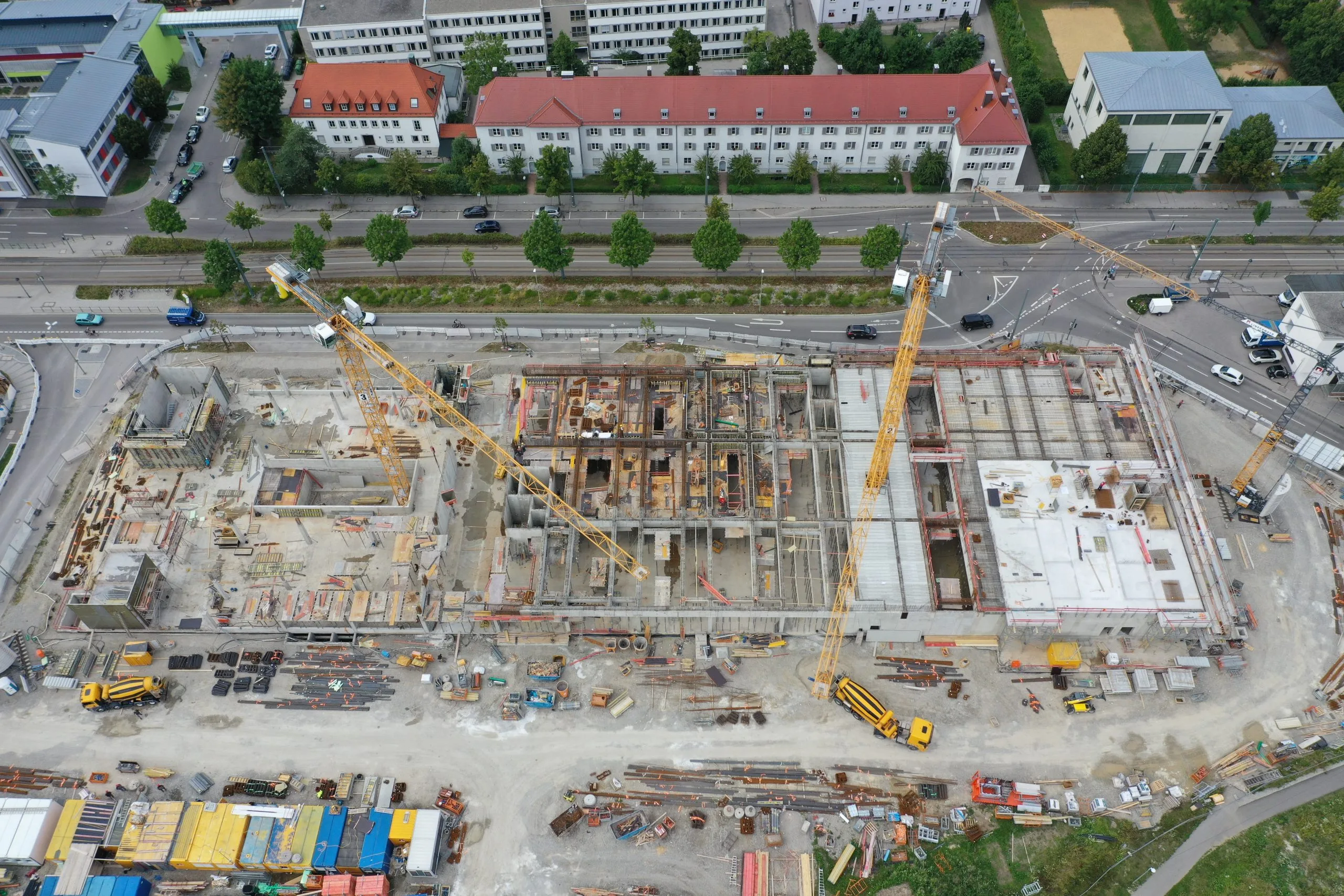Blick von oben auf einen Rohbau mit Betonwänden und mehreren Baukränen an einer Straßenkreuzung.