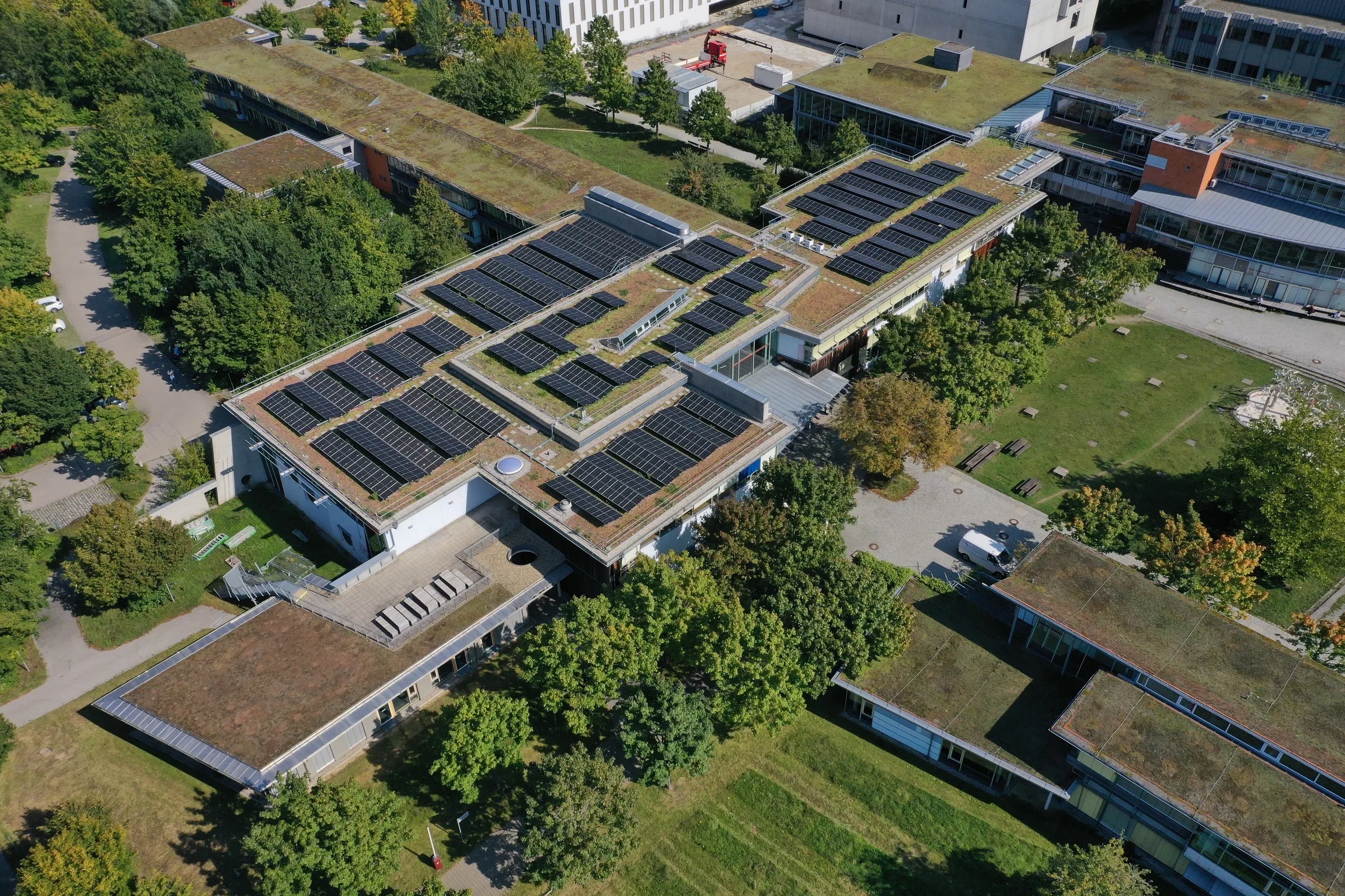 Luftaufnahme eines Gebäudekomplexes mit begrünten Flachdächern und Photovoltaikanlagen.