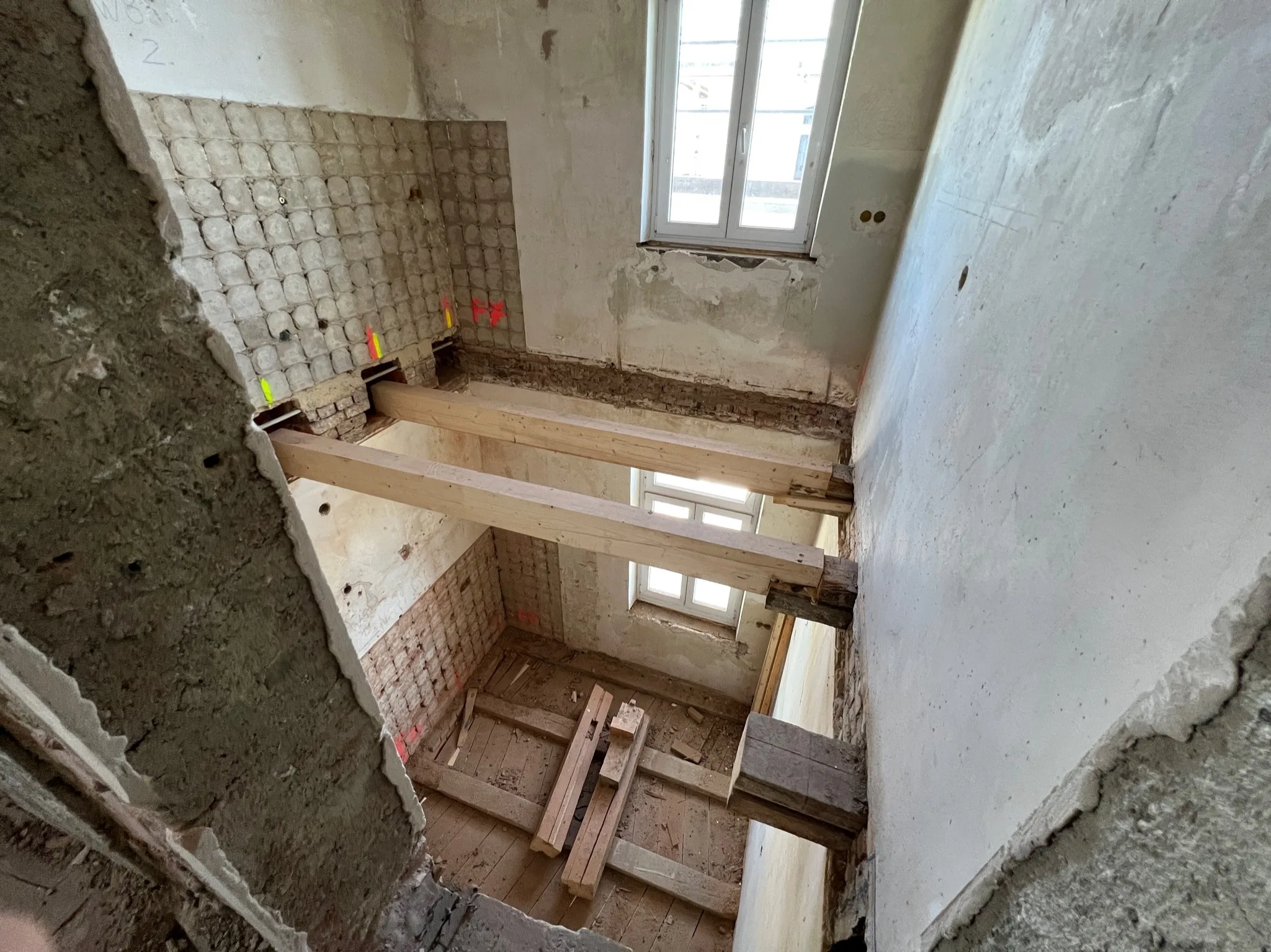Geöffnete Geschossdecken in einem Bestandsgebäude mit freigelegtem Mauerwerk und provisorischen Holzbalken.